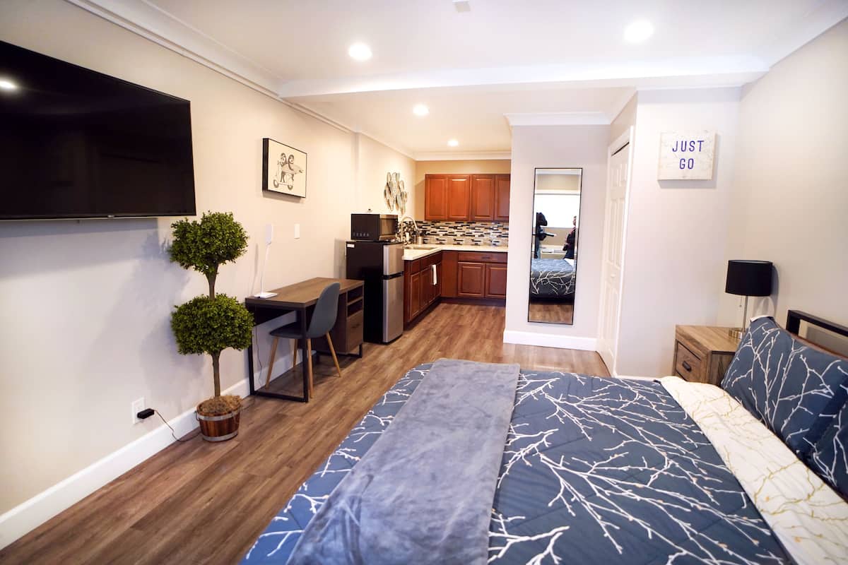 A compact living space with a bed, a desk, a small kitchen, and a TV.