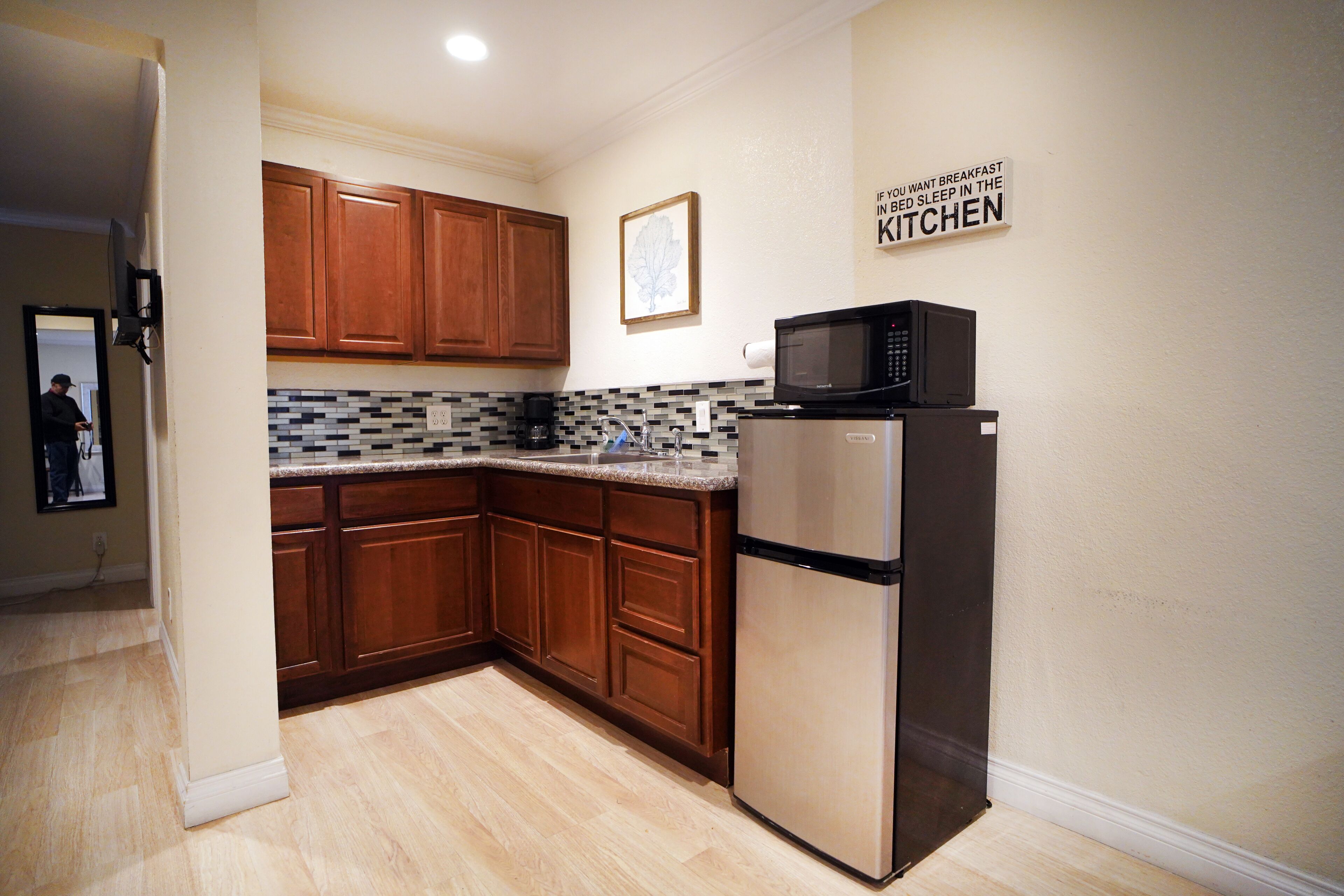 A kitchen with wooden cabinets, a stainless steel refrigerator, a microwave, and a tiled backsplash.