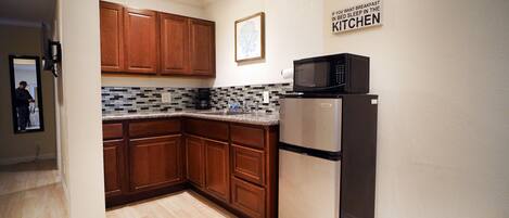 A kitchen with wooden cabinets, a stainless steel refrigerator, a microwave, and a tiled backsplash.