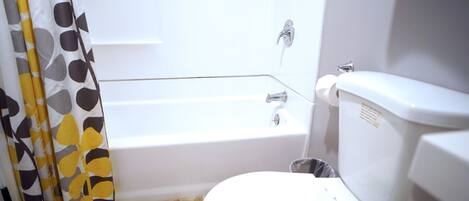 Un baño con inodoro blanco, bañera y cortina de ducha con diseño geométrico.
