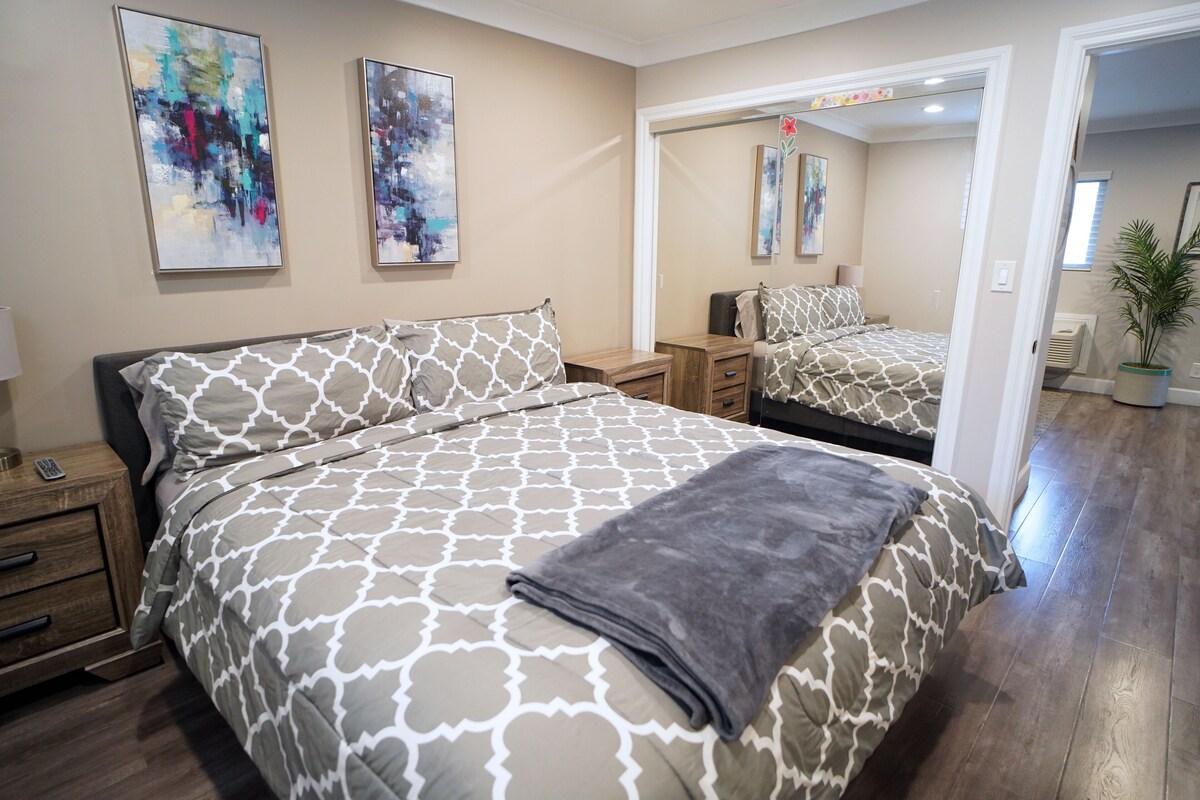 A bedroom with a large bed, a nightstand, a dresser, and a mirror.