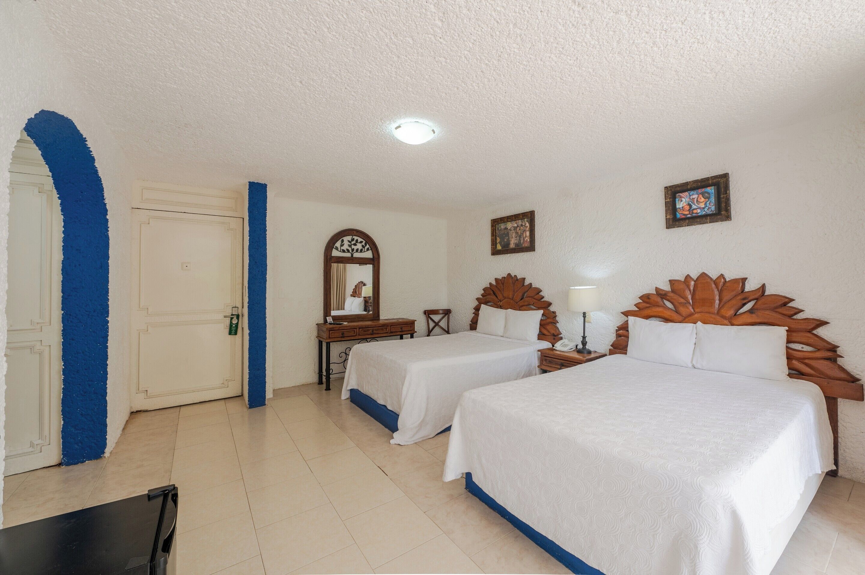 A hotel room with two beds, a desk, a chair, a mirror, and a picture on the wall.