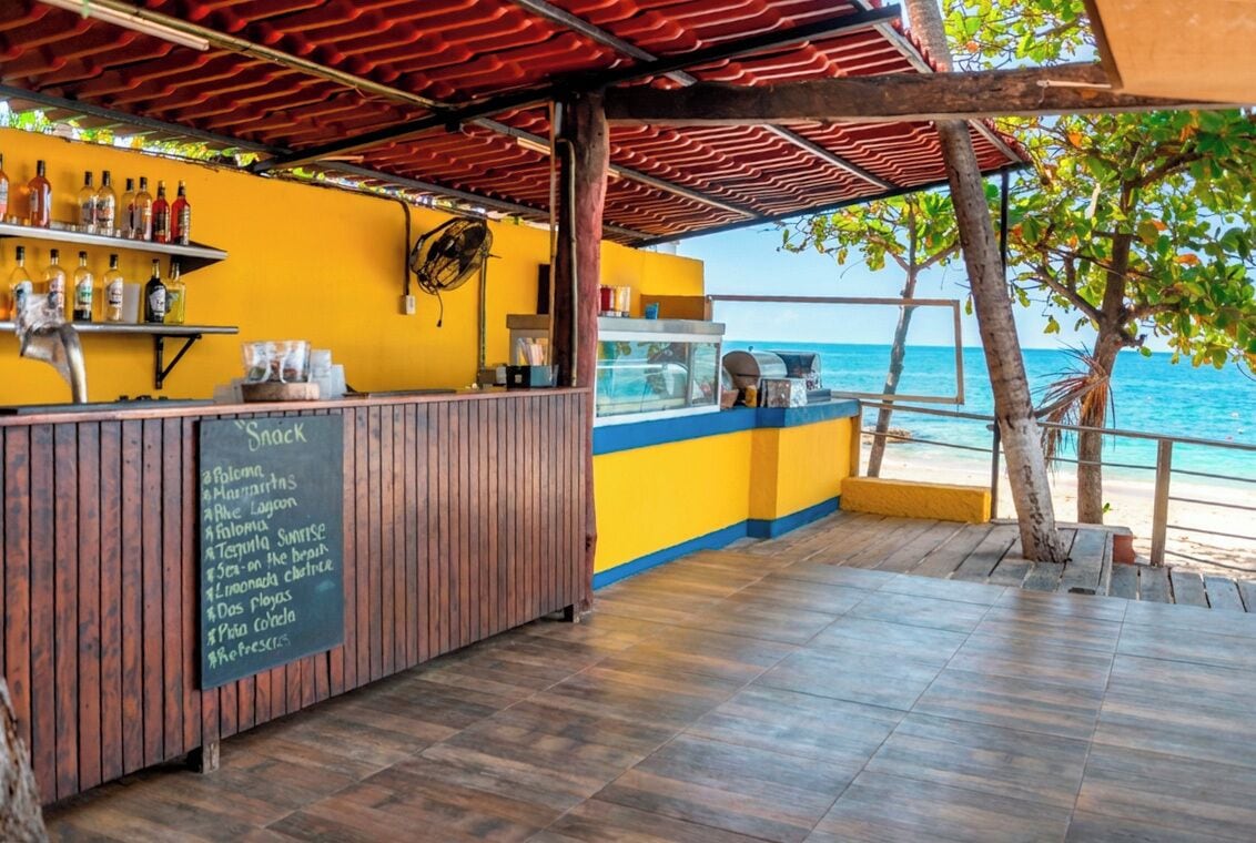 En bar ved stranden med en trædisk, en tavle med menu og udsigt over havet.