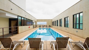 An indoor swimming pool with clear blue water, surrounded by lounge chairs and a high ceiling. - Comfort Hotel Taguatinga (Taguatinga)