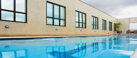A swimming pool with clear blue water, surrounded by a brick building with large windows.