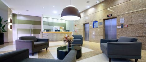 A modern lobby with a reception desk, seating area, and elevators.