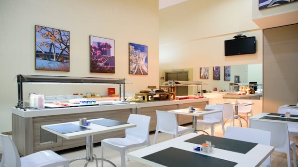 A modern cafe with a buffet counter, white chairs, and artwork on the walls. - Comfort Hotel Taguatinga (Taguatinga)