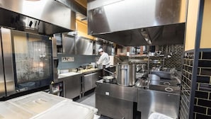 Una cocina comercial con electrodomésticos de acero inoxidable, un chef trabajando y una amplia cámara frigorífica para hielo.