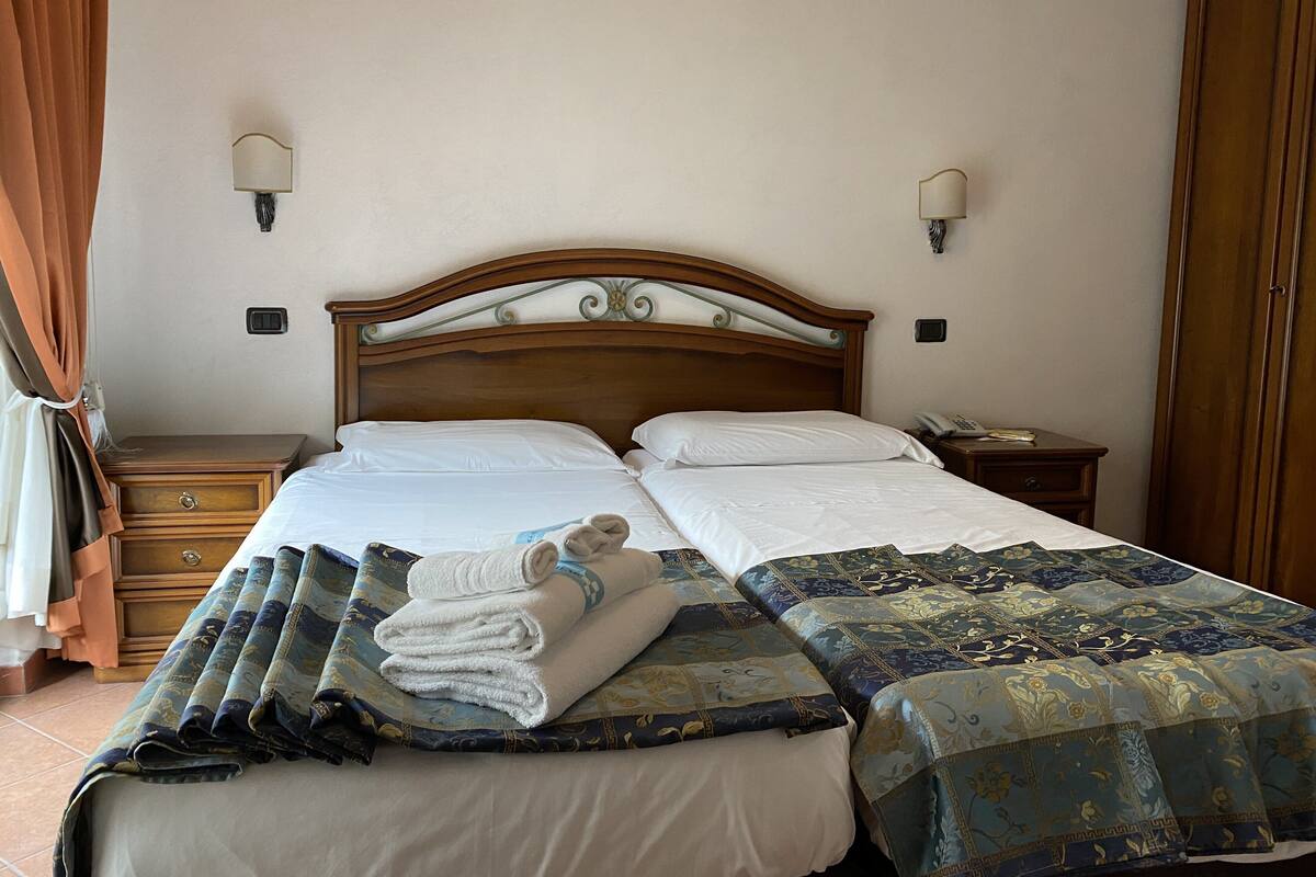 Una cama doble con ropa blanca, cabecera de madera, dos mesitas de noche y colcha estampada.
