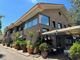 A two-story building with large windows, a brick facade, and a covered outdoor seating area with potted plants.