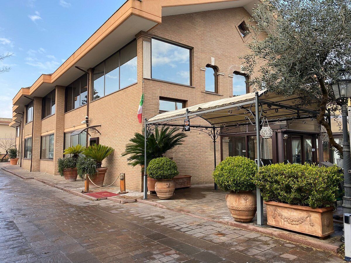 A modern hotel with a brick facade, large windows, and a covered entrance area with potted plants.