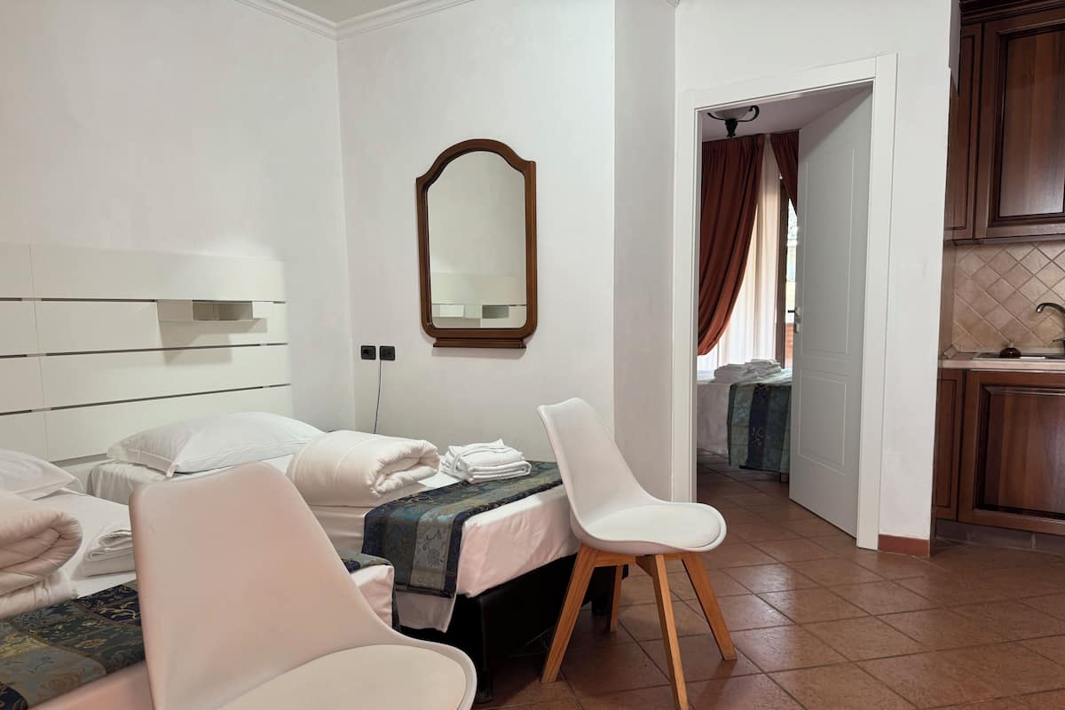 Habitación de hotel con cama, dos sillas, un espejo y vistas a la cocina.