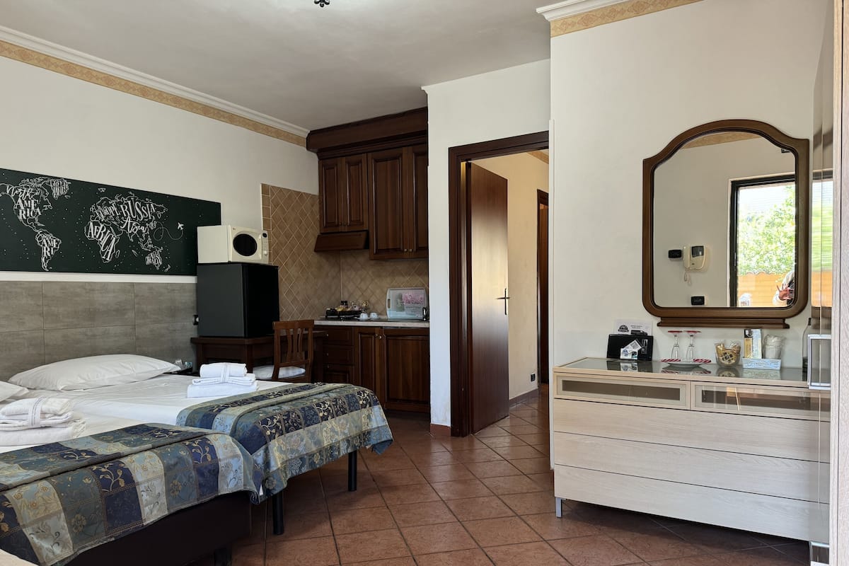 Habitación de hotel con dos camas, kitchenette, un espejo grande y un mapa del mundo en la pared.