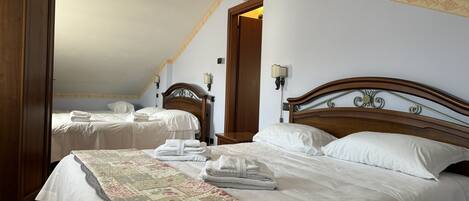 A hotel room with two beds, each with white linens and a floral-patterned bedspread. There are two wall-mounted lamps and a wooden wardrobe.