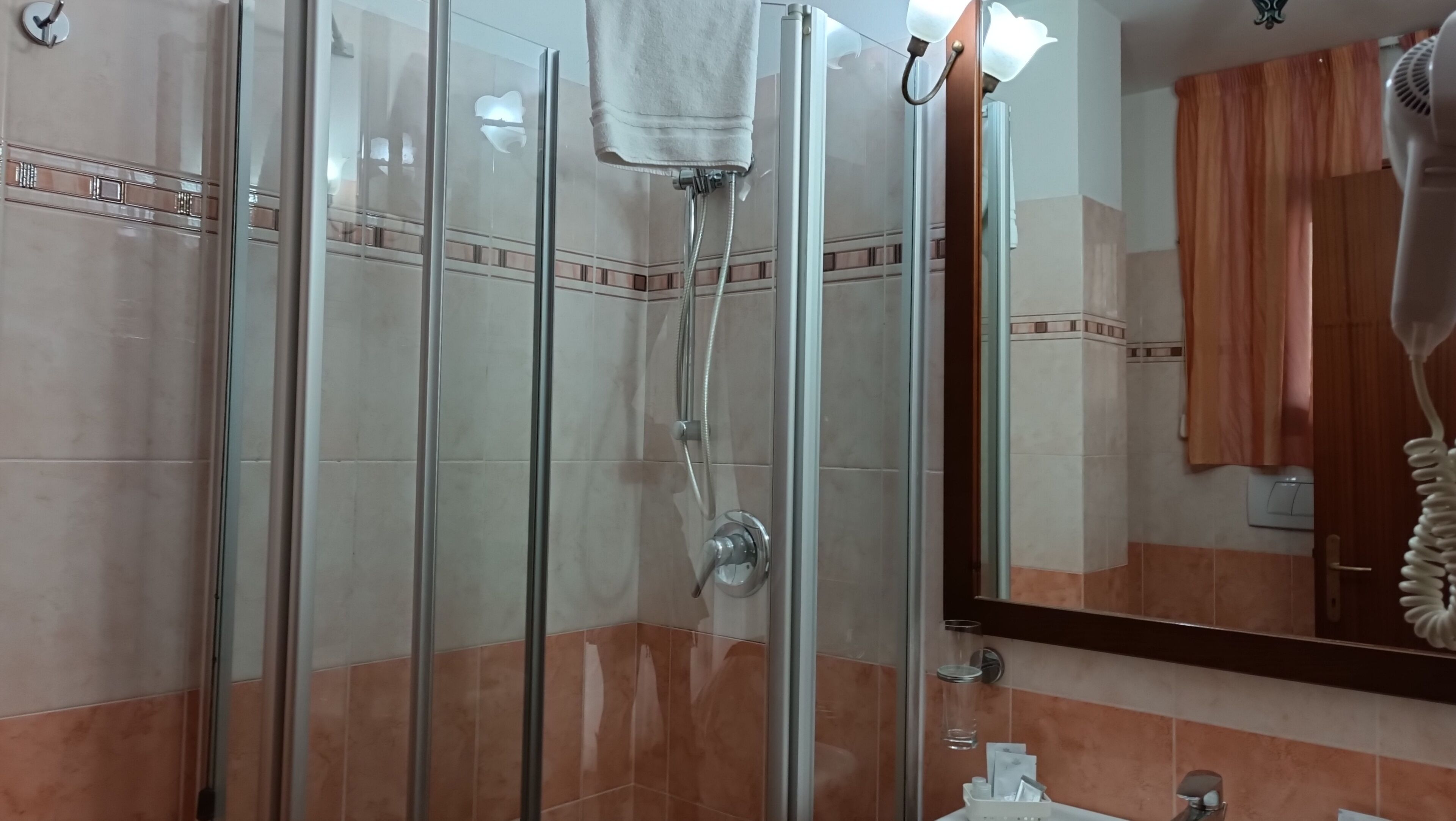 Ducha con mampara de vidrio, una toalla colgada en la puerta, un espejo y un lavabo con un perchero para toallas.