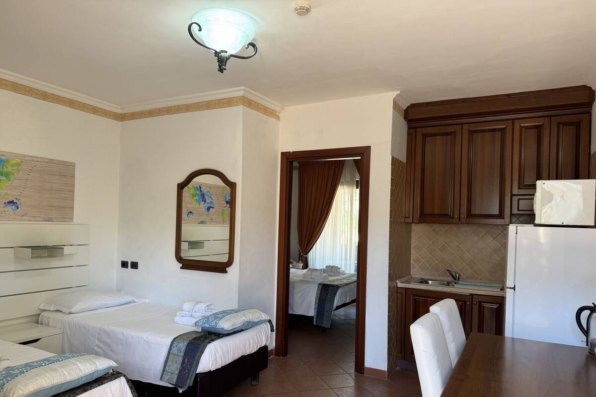 Ein Hotelzimmer mit zwei Betten, einer kleinen Küchenzeile und einem durchgehenden Türrahmen sichtbaren Badezimmer.