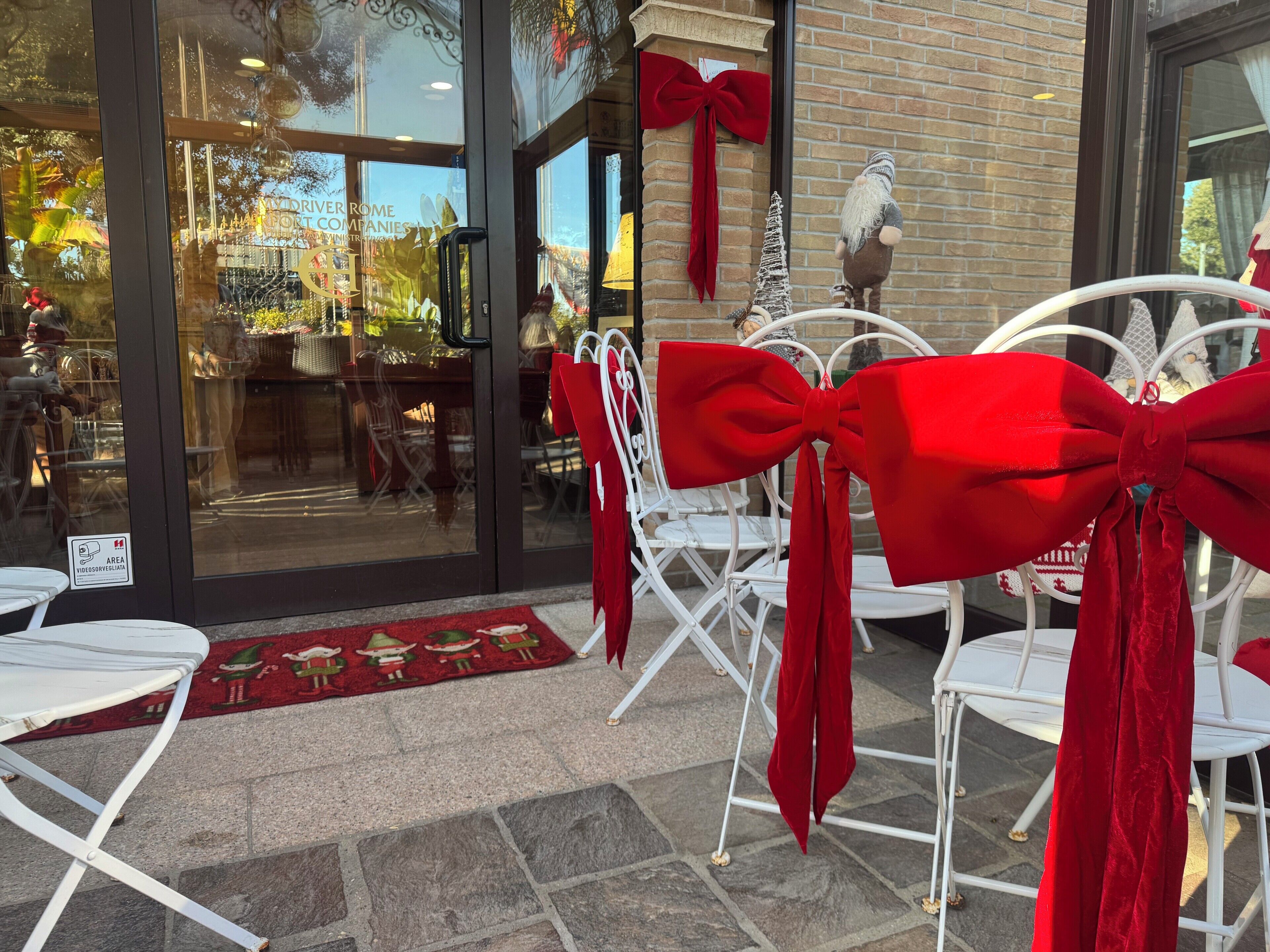 A restaurant entrance with red bows on chairs, a Christmas tree, and a Santa Claus decoration.