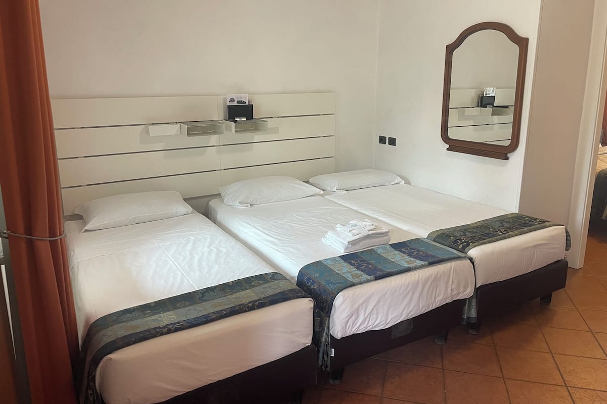 Habitación de hotel con dos camas individuales, una mesita de noche, un espejo y un estante pequeño con un teléfono y una caja.