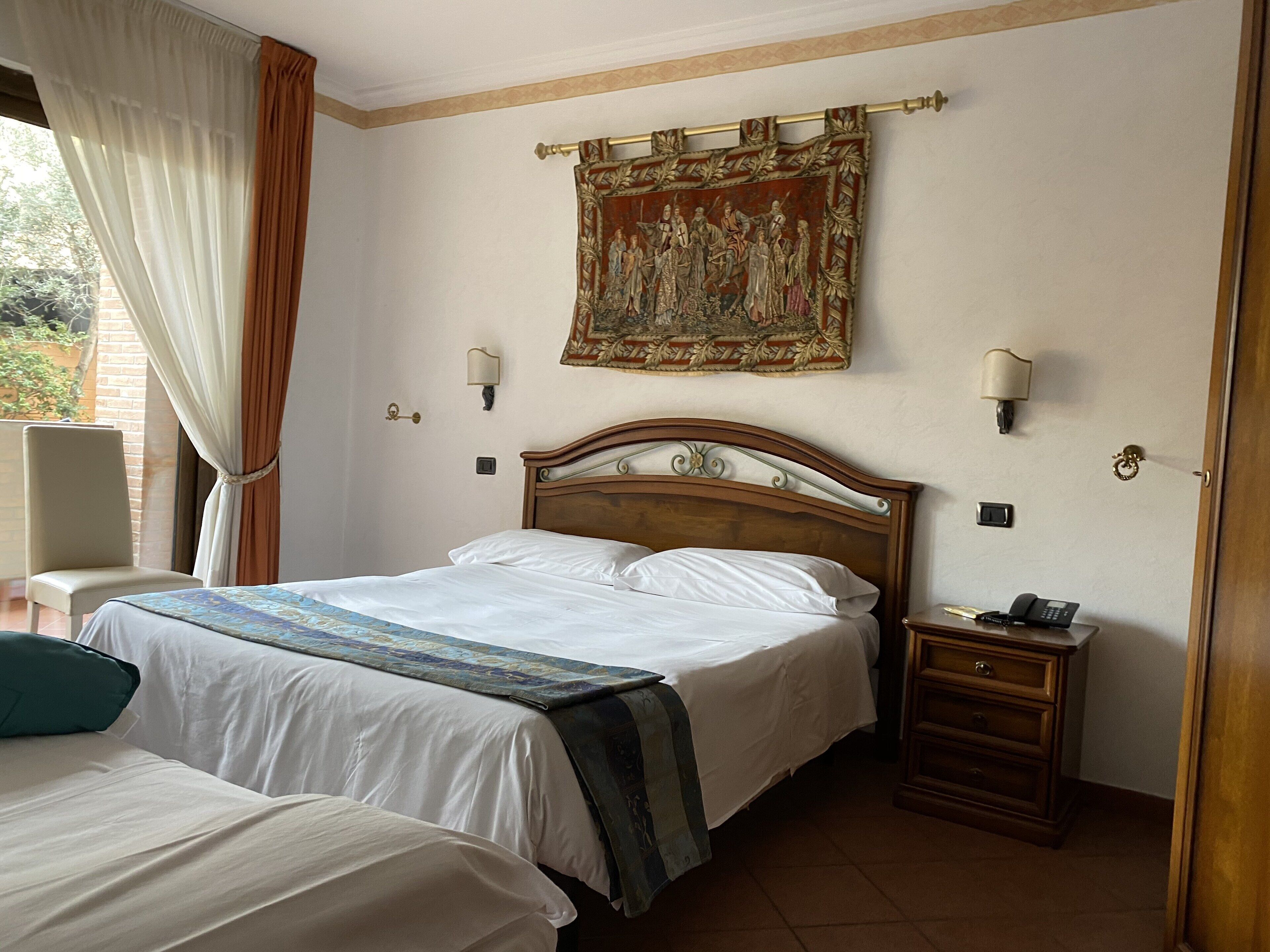 A hotel room with a large bed, a smaller bed, a nightstand with a phone, and a tapestry on the wall.