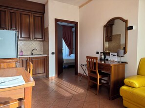 Ein kleines Hotelzimmer mit Küchenzeile, Schreibtisch, Stuhl und Bett.