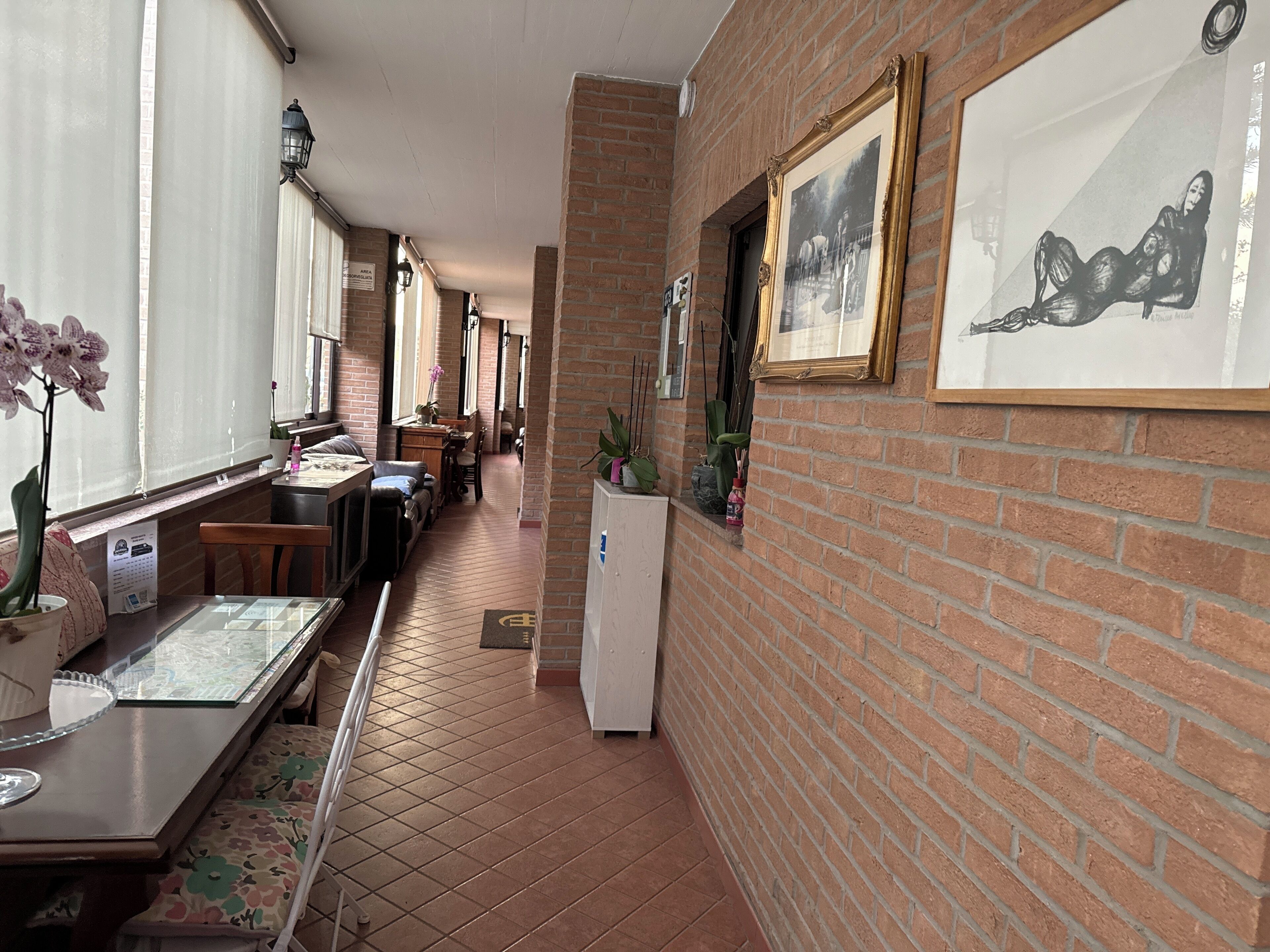 A corridor with a brick wall, a refrigerator, and framed pictures on the wall.