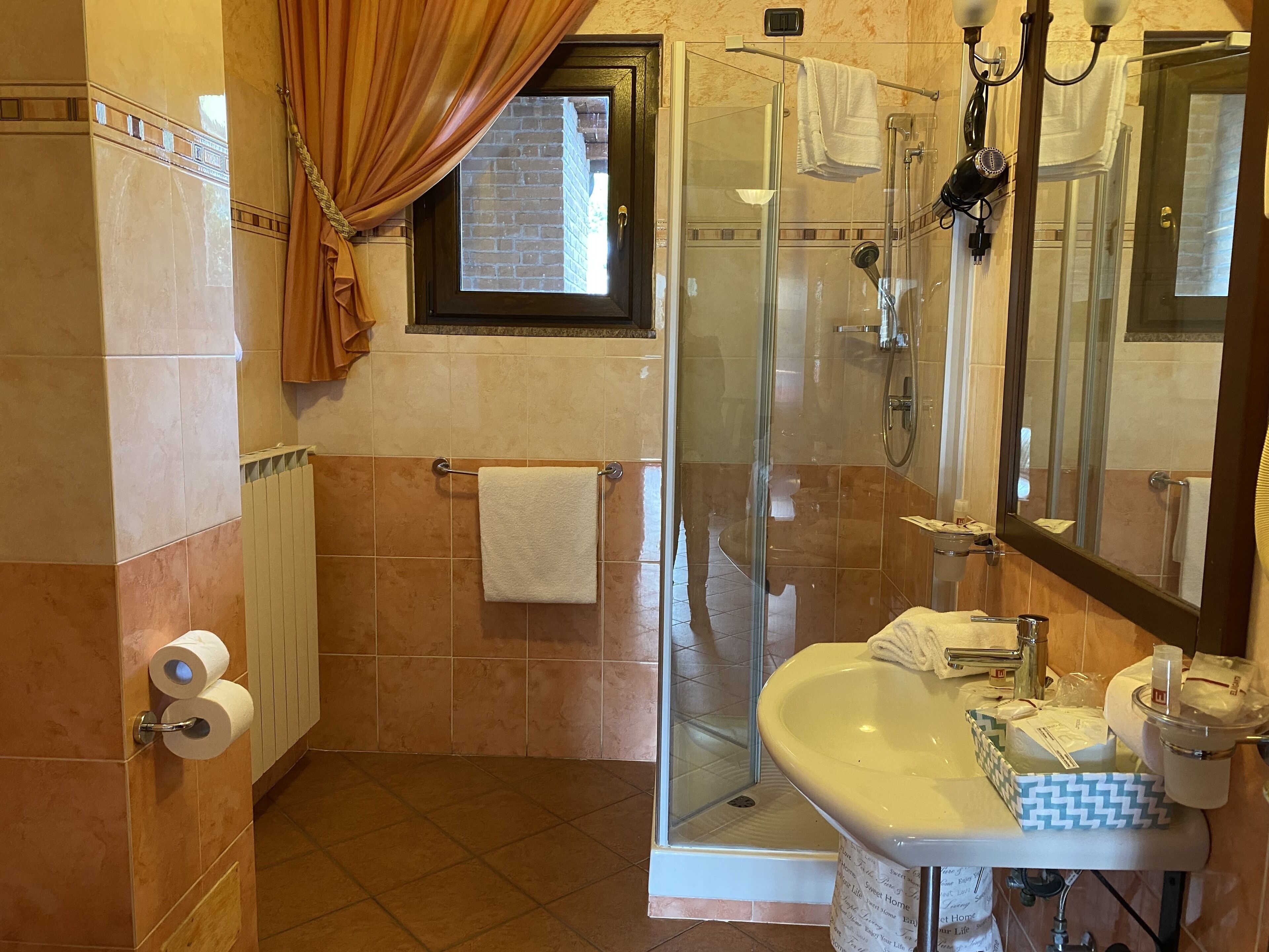 Een badkamer met een douchecabine van glas, een wastafel met toiletartikelen en een handdoekrek.