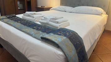 Un letto rifatto con cura, una coperta a motivi decorativi, un asciugamano bianco piegato e una lampada da comodino.