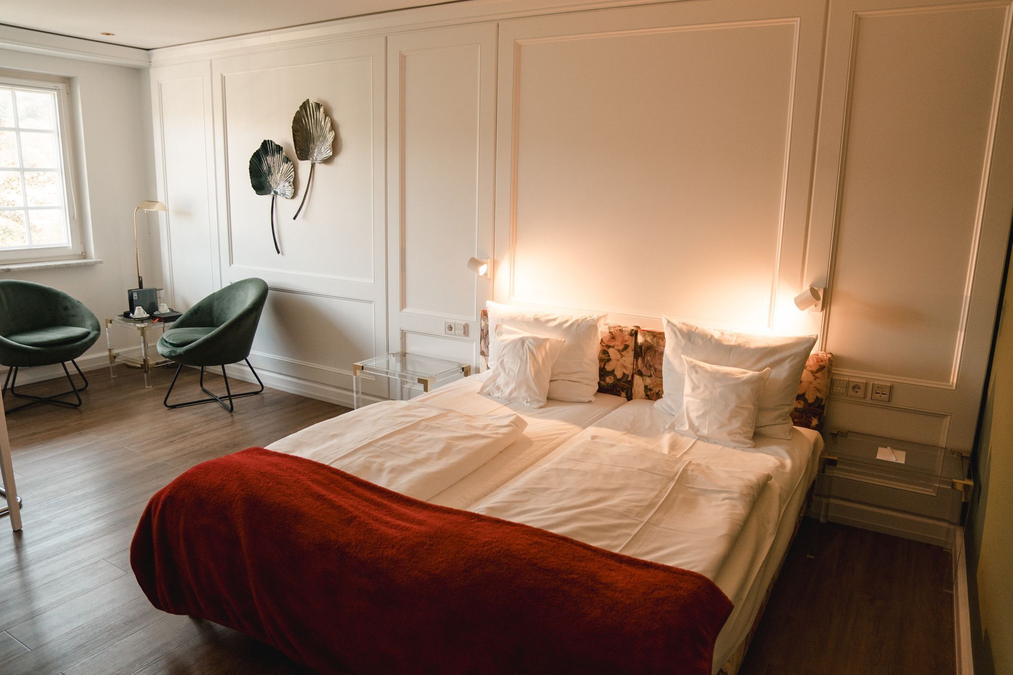 A bedroom with a large bed, two chairs, a desk, and decorative wall art.