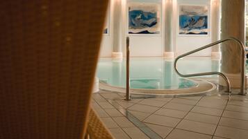Ein Hallenbad mit klarem Wasser, umgeben von gefliestem Boden und Metallgeländern.