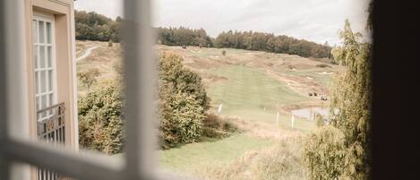 Une vue depuis une fenêtre donnant sur un terrain de golf, avec un bâtiment sur la gauche.