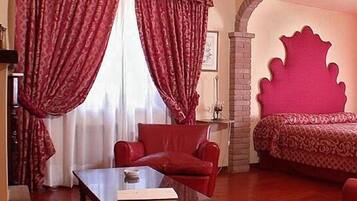 A room with a red sofa, a wooden coffee table, a patterned bedspread, and a large red headboard.