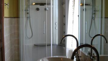 Un baño con ducha envuelta en vidrio, dos lavamanos y un espejo.