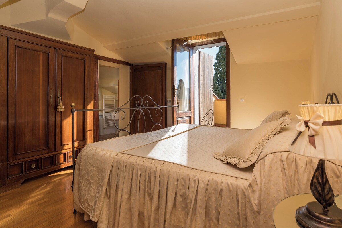 A bedroom with a large bed, wooden wardrobe, and a balcony with a view of trees.
