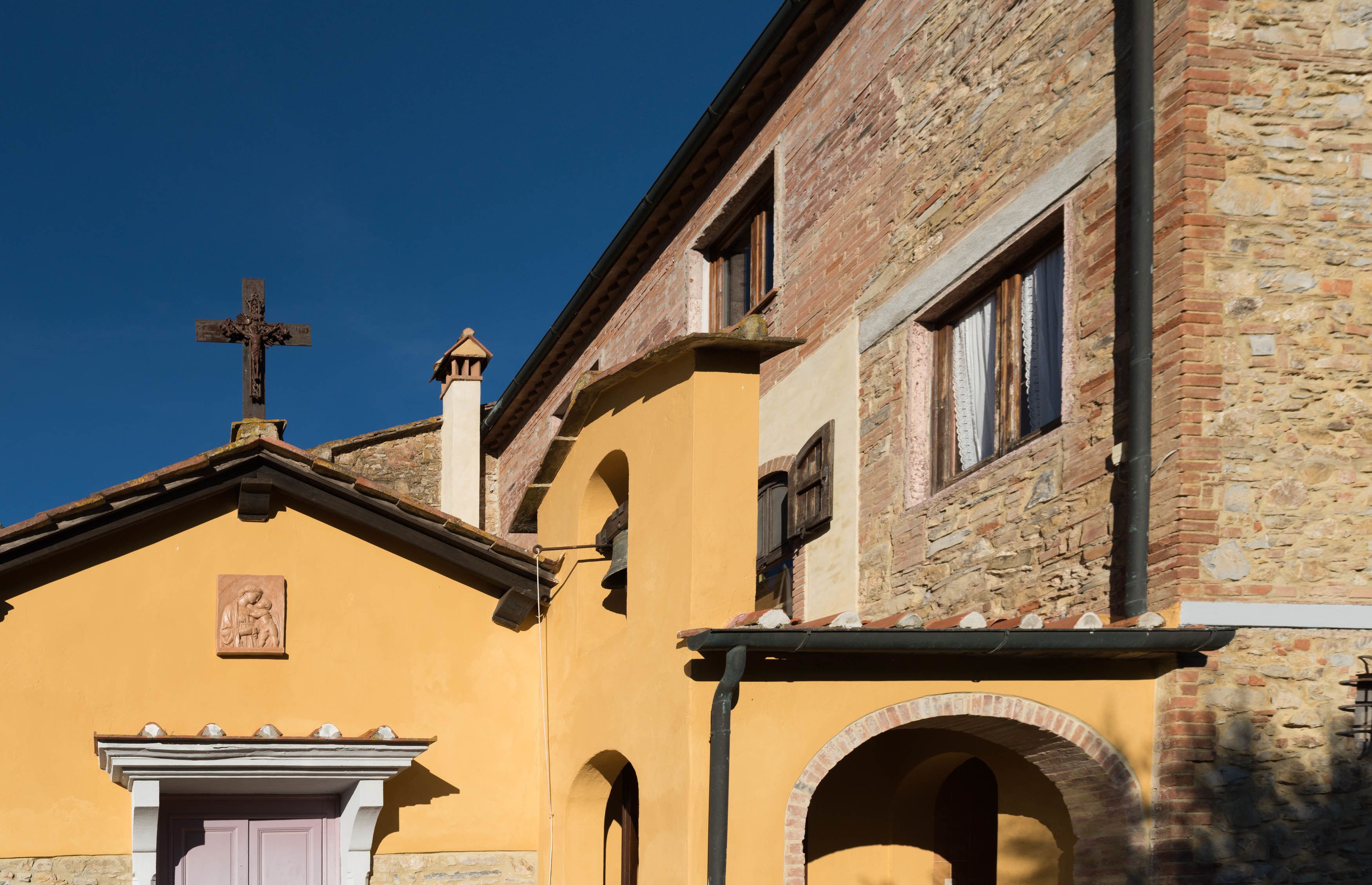 Un bâtiment surmonté d’une croix, doté d’une façade en pierre et d’un mur jaune.