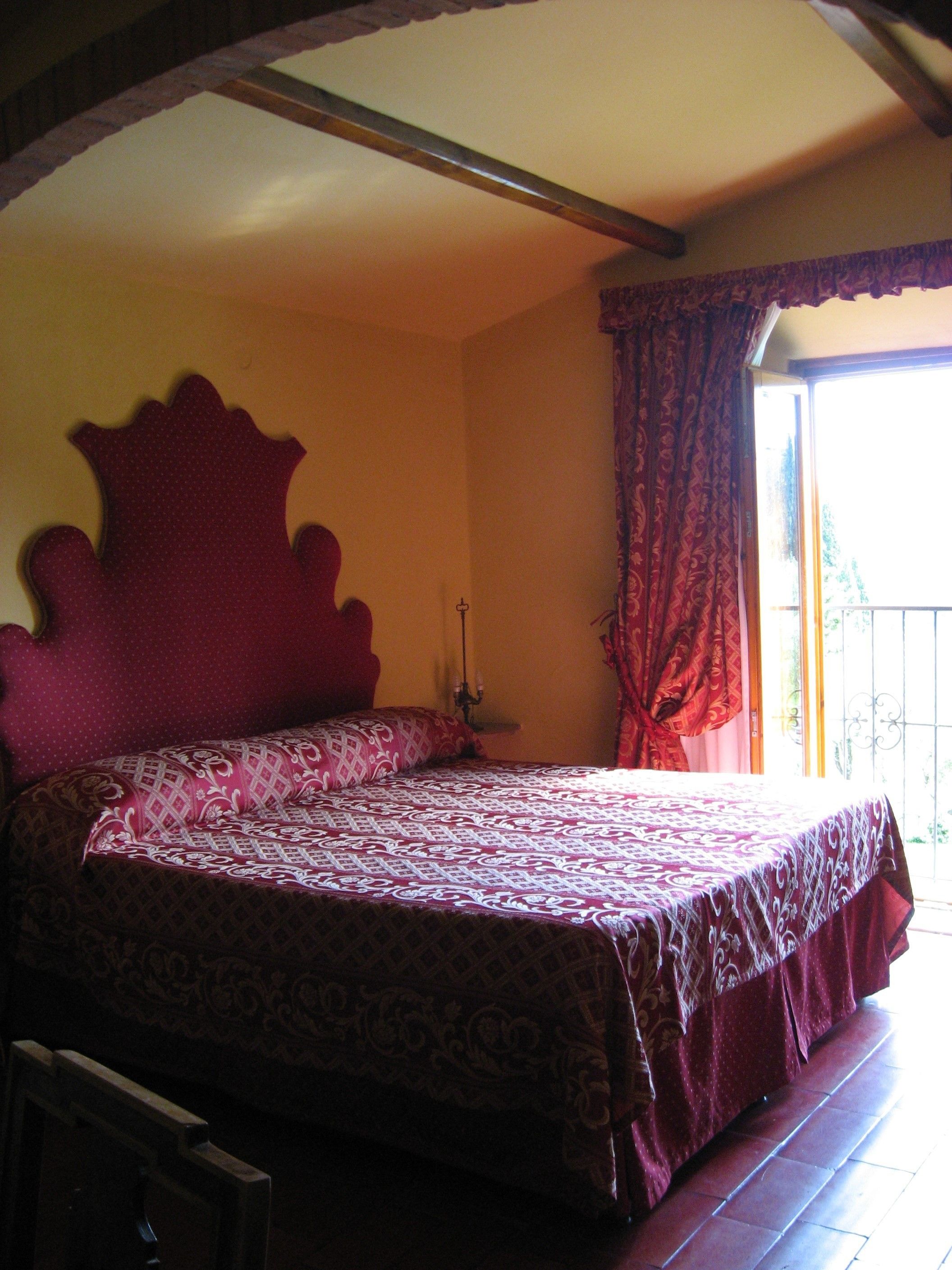 A bedroom with a large bed, a nightstand, and a window with curtains.