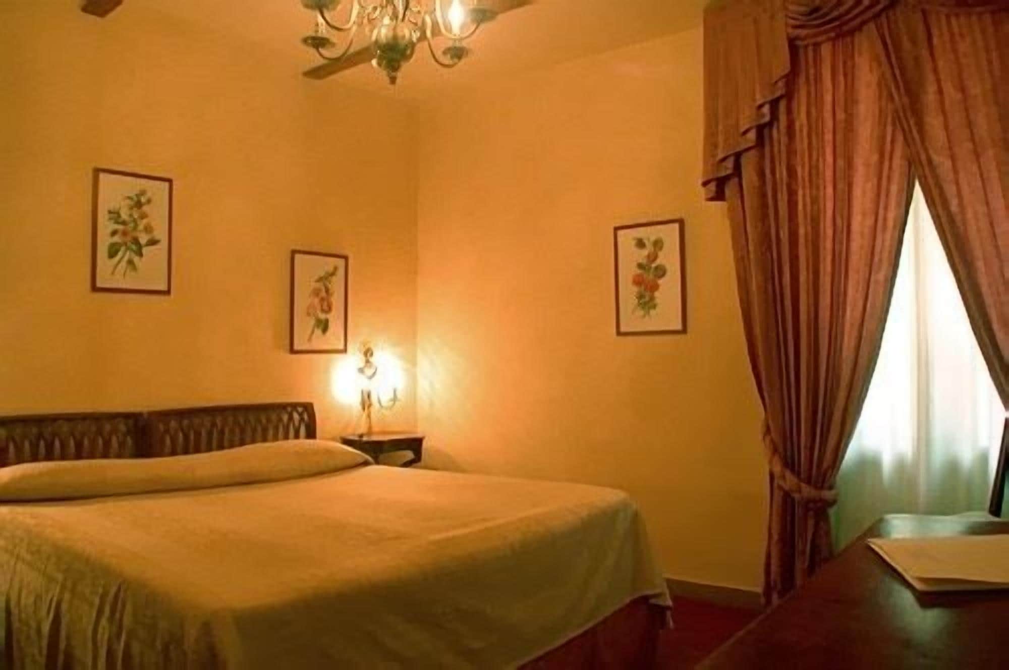Ein Zimmer mit einem Bett, einem Nachttisch, einer Chandelüster und gerahmten Blumenbildern an den Wänden.