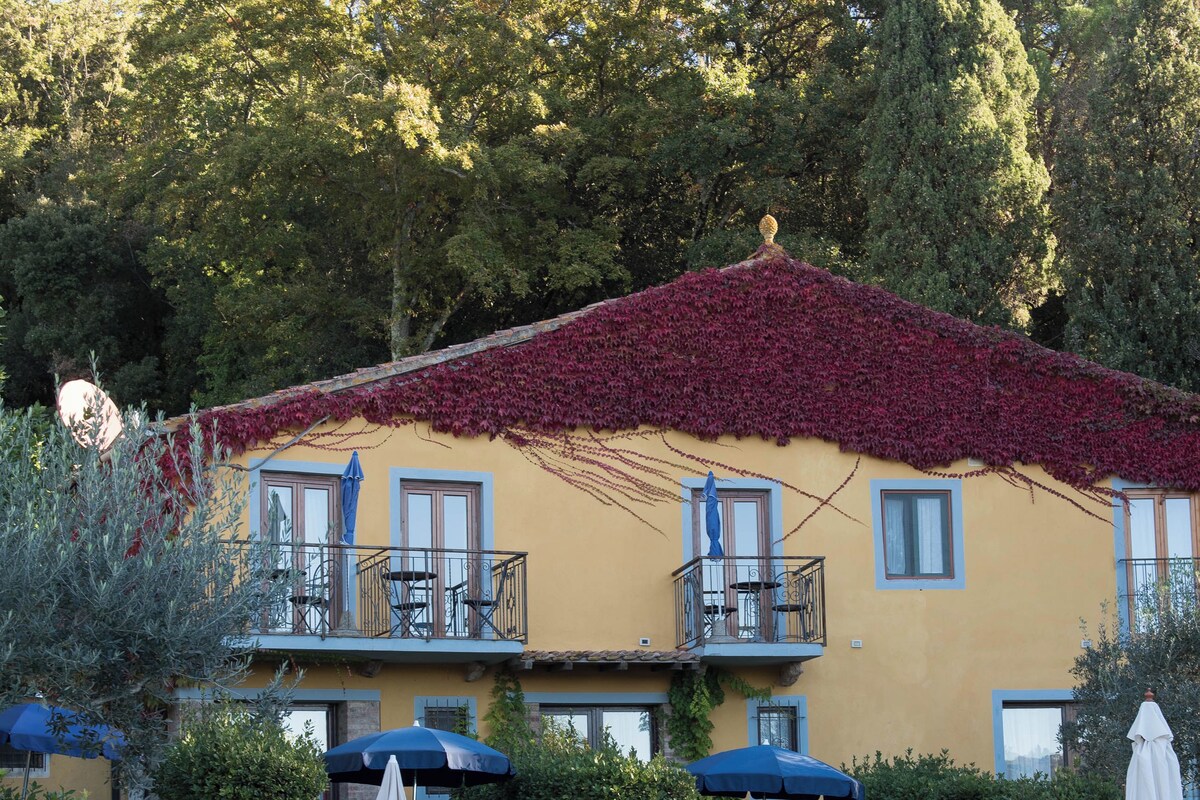 A yellow building with a red roof, a swimming pool, and lounge chairs.