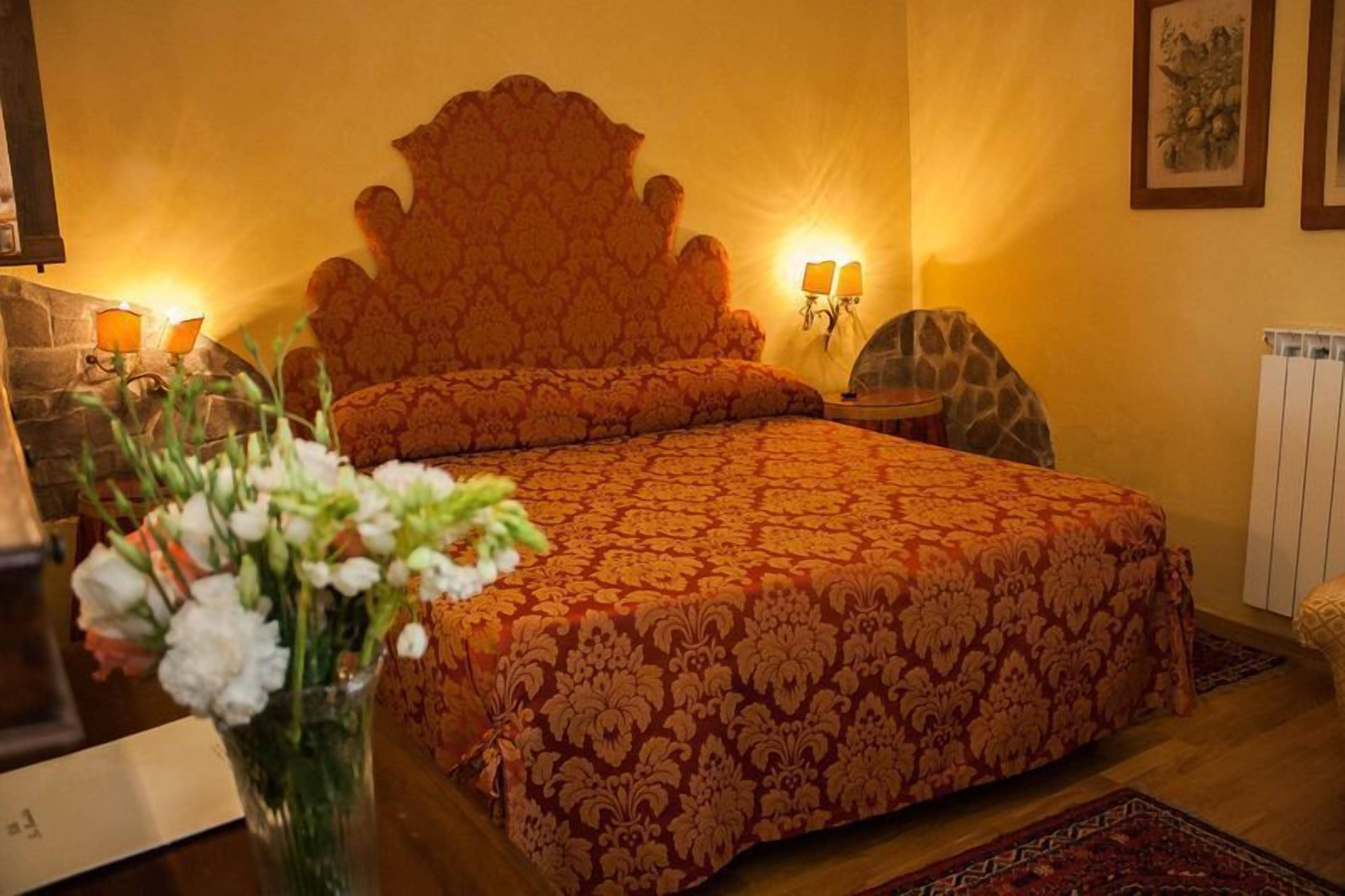 Ein Schlafzimmer mit einem großen Bett, einem Nachttisch mit Lampe, einem Sessel und einer Blumenvase.