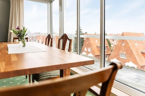 A dining table with chairs, a vase with flowers, and a view of buildings through large windows. - Best Western Hotel Heide (Oldenburg)