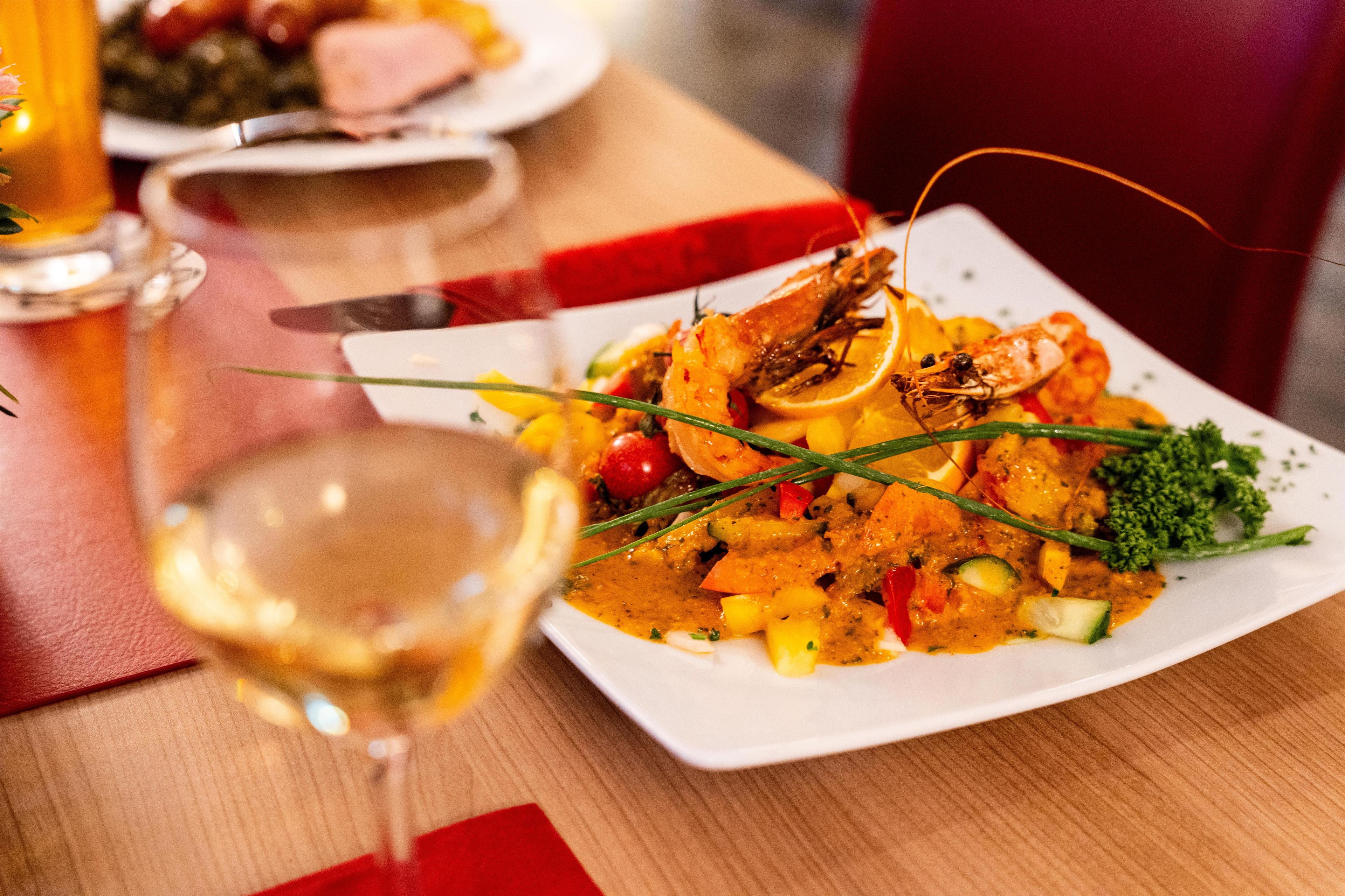 Une table à manger avec une assiette de nourriture, un verre de vin blanc et une chaise rouge.