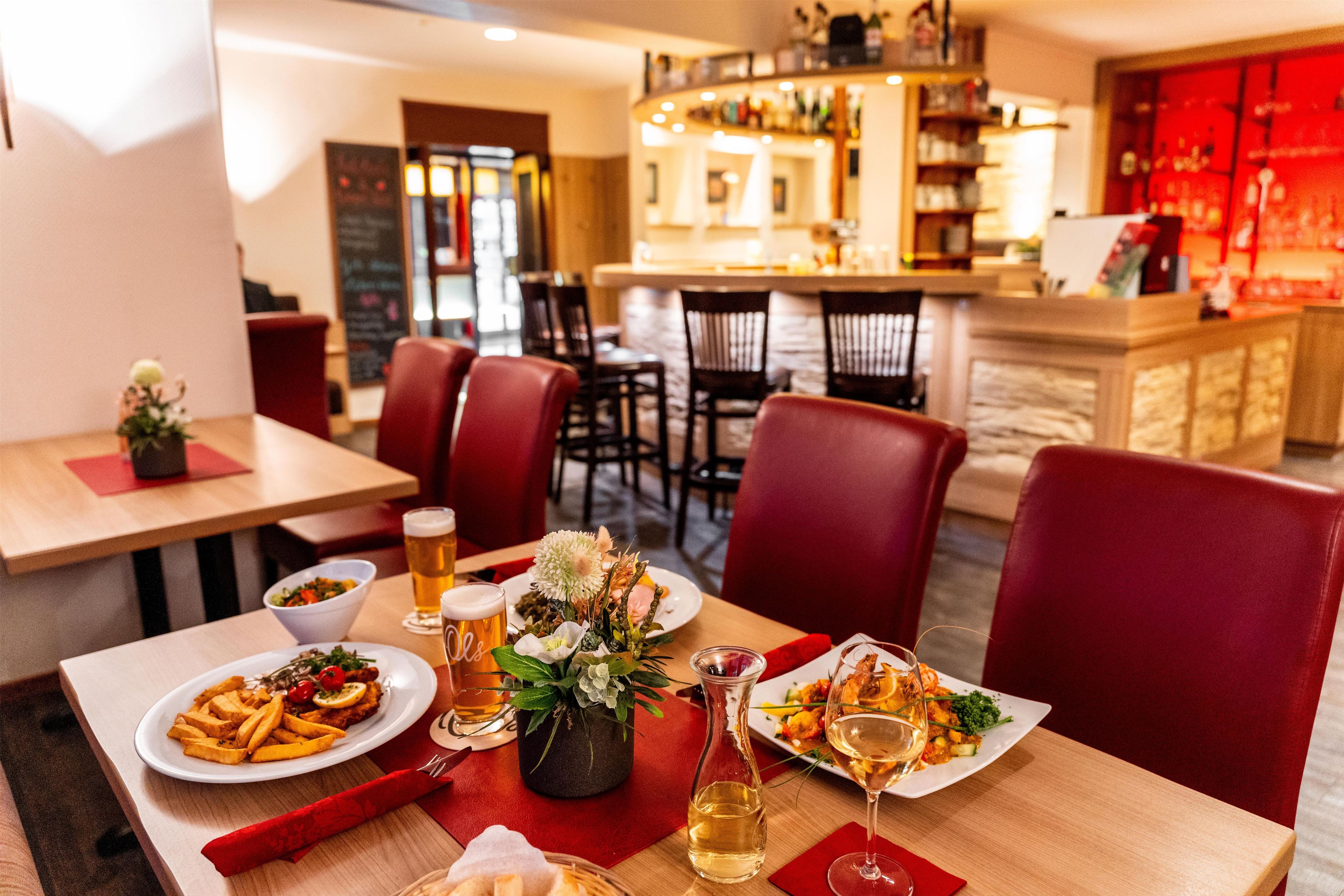 A restaurant interior with tables set for dining, a bar area in the background, and a flower centerpiece on the table.
