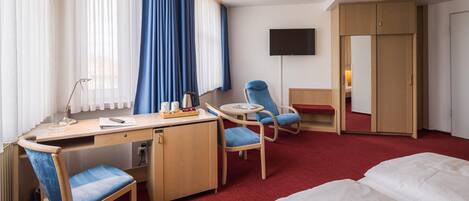 Une chambre d’hôtel équipée d’un bureau, de deux chaises, d’un lit, d’une télévision et d’une armoire.