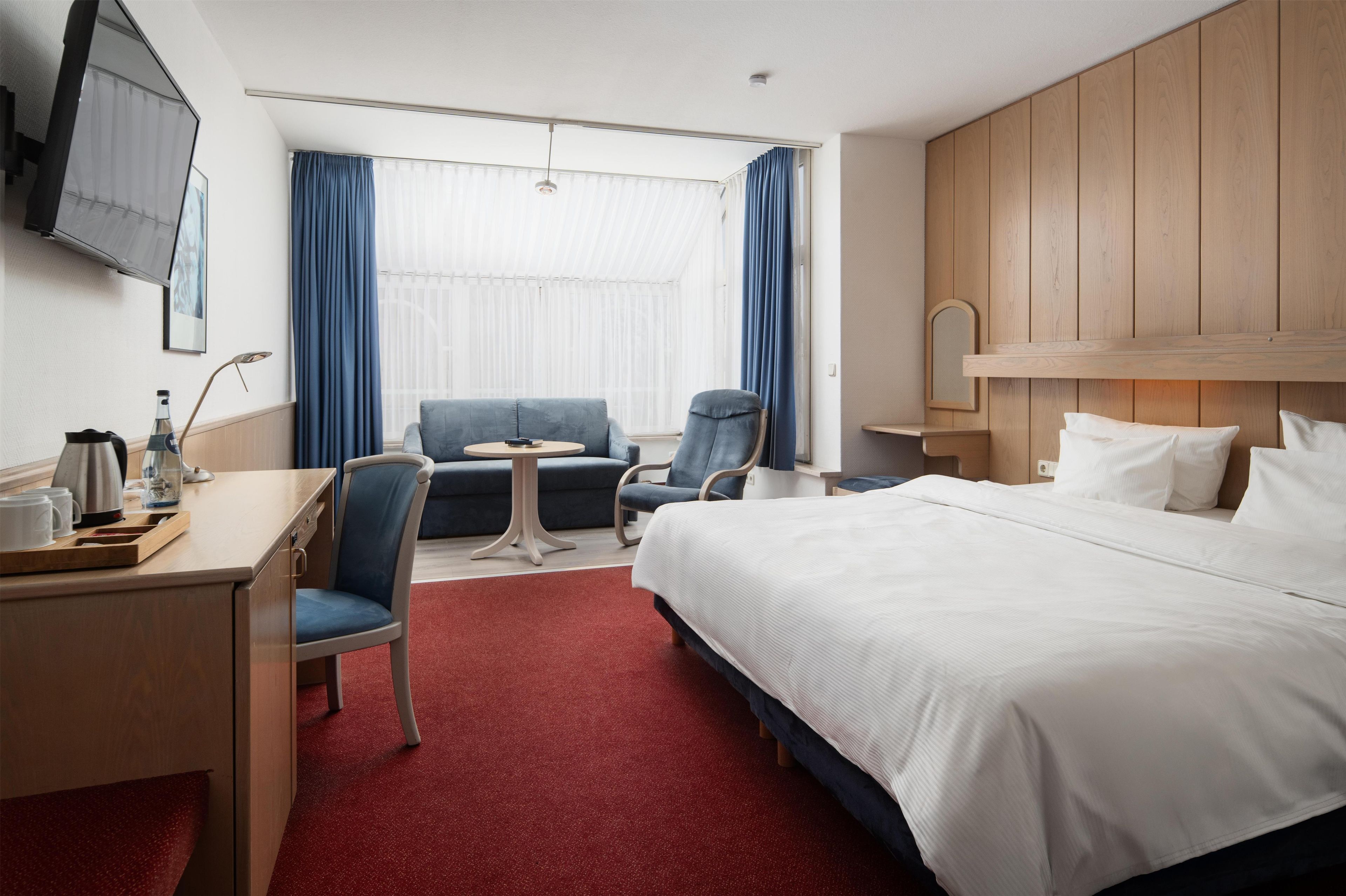 Hotellihuone, jossa on sänky, työpöytä, tuoli, pieni pöytä ja televisio.