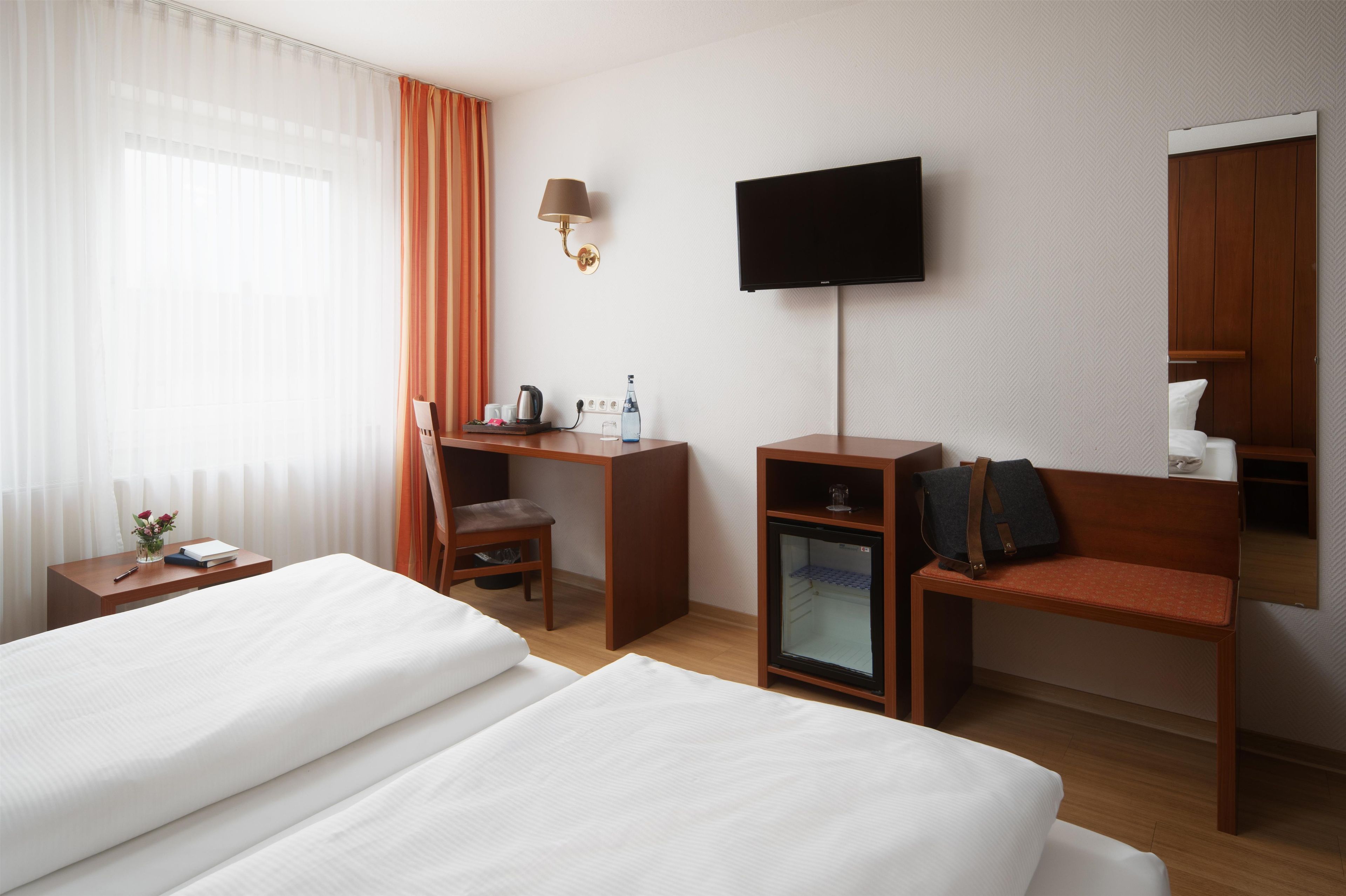 A hotel room with two beds, a desk, a chair, a television, and a minibar.