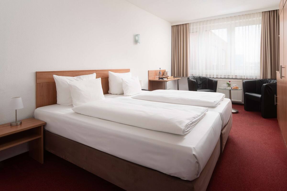 Habitación de hotel con dos camas, un escritorio, una silla y una pequeña mesa con lámpara.