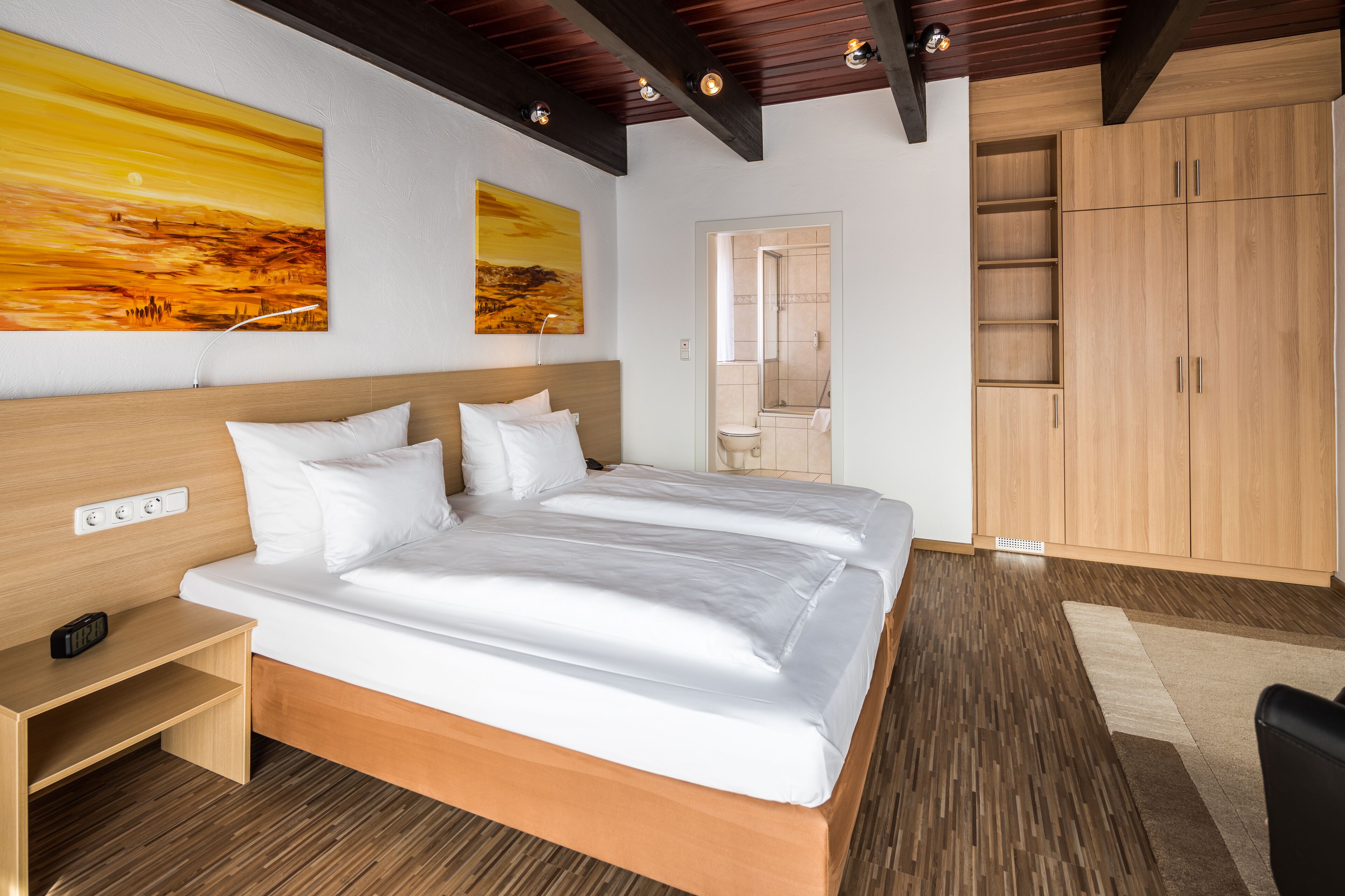Ein modernes Hotelzimmer mit einem Holzbett, weißen Bettwäsche, einem Holzschrank und zwei Landschaftsbildern an der Wand.