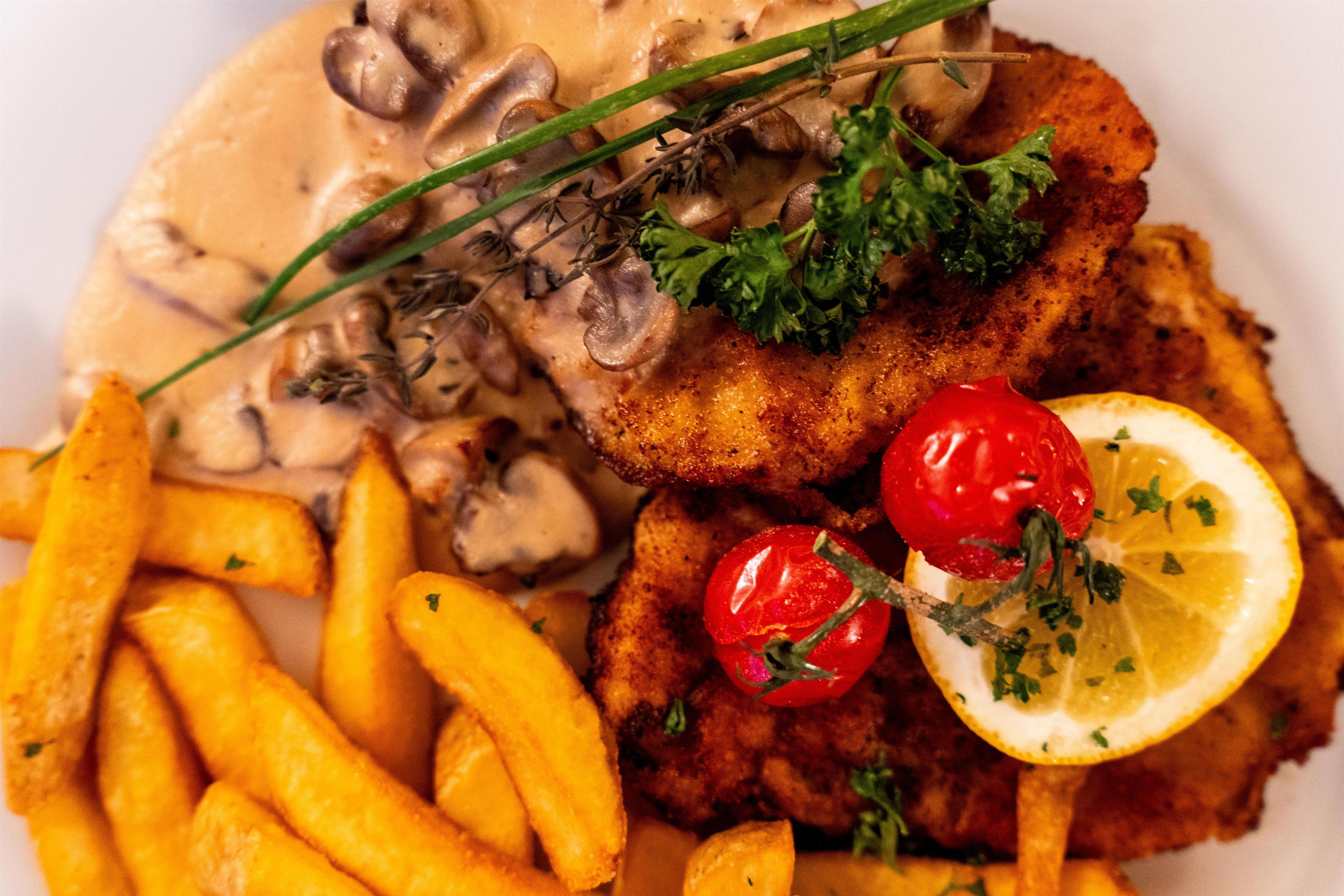 Une assiette comprenant une escalope panée, des champignons, des tomates cerises, un quartier de citron et des frites.