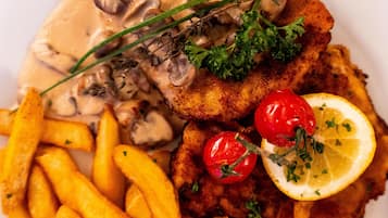 Une assiette comprenant une escalope panée, des champignons, des tomates cerises, un quartier de citron et des frites.