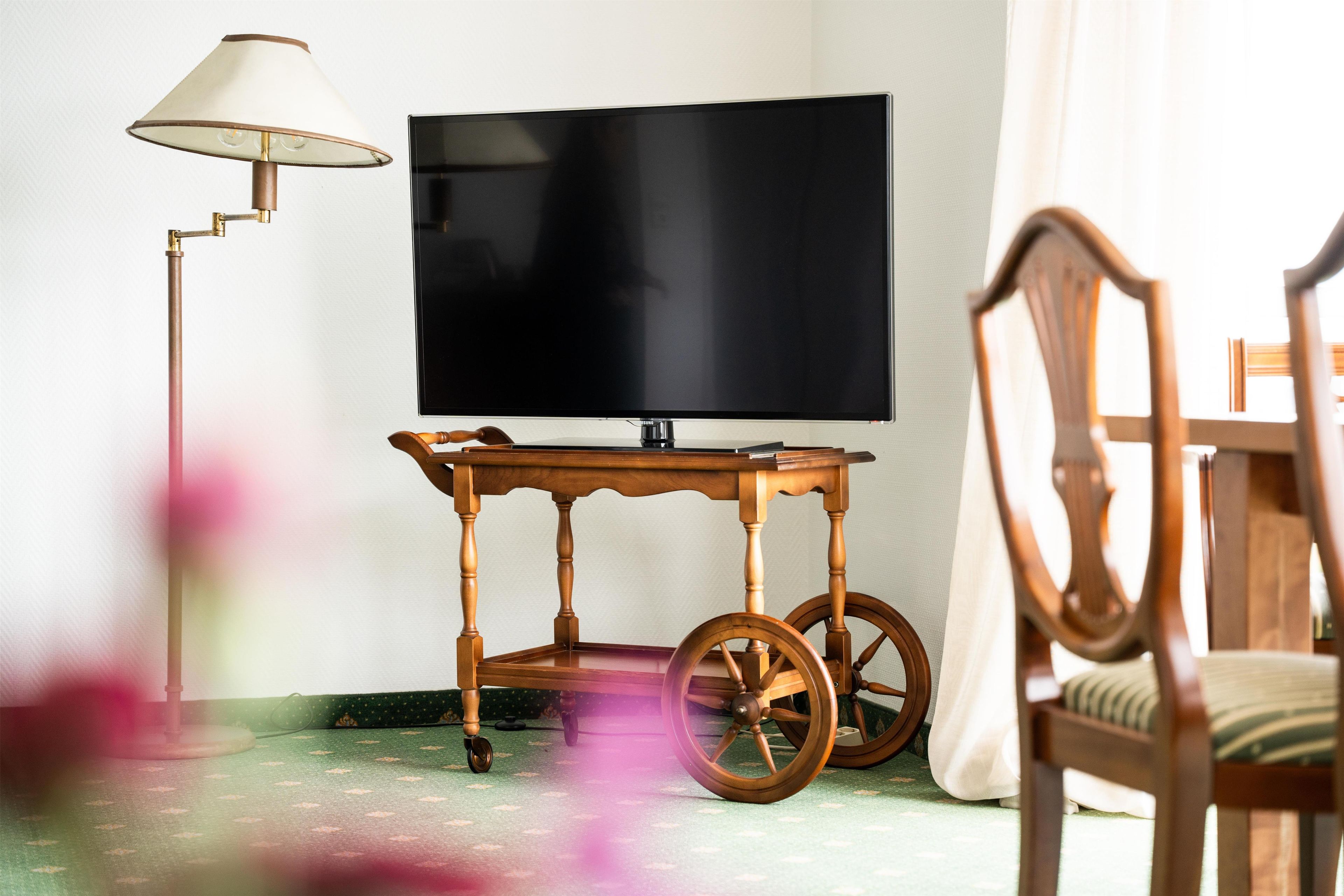 A room with a television on a wooden stand, a floor lamp, and a chair.