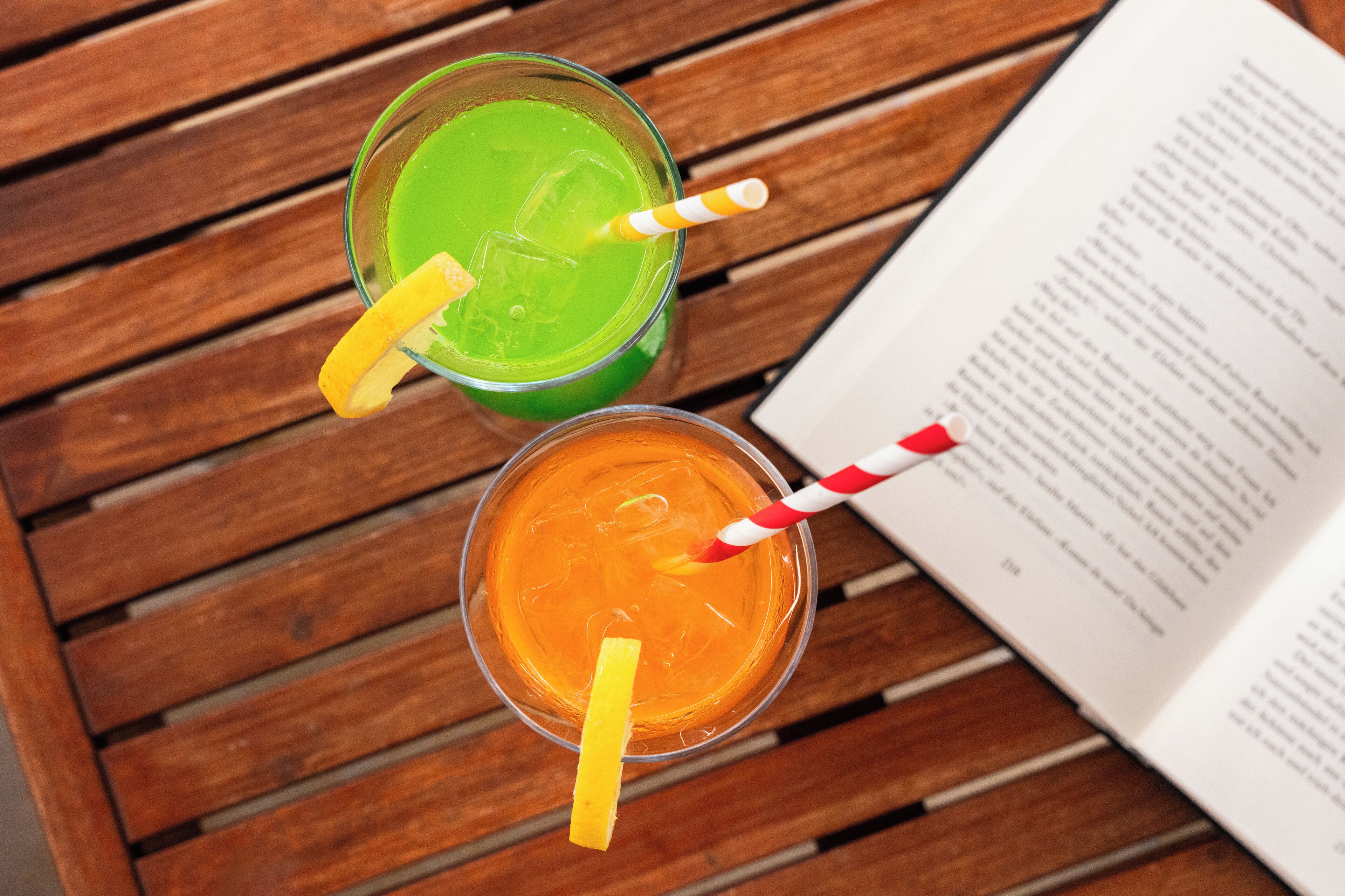 Dos bebidas con pajitas y rodajas de limón sobre una mesa de madera junto a un libro abierto.